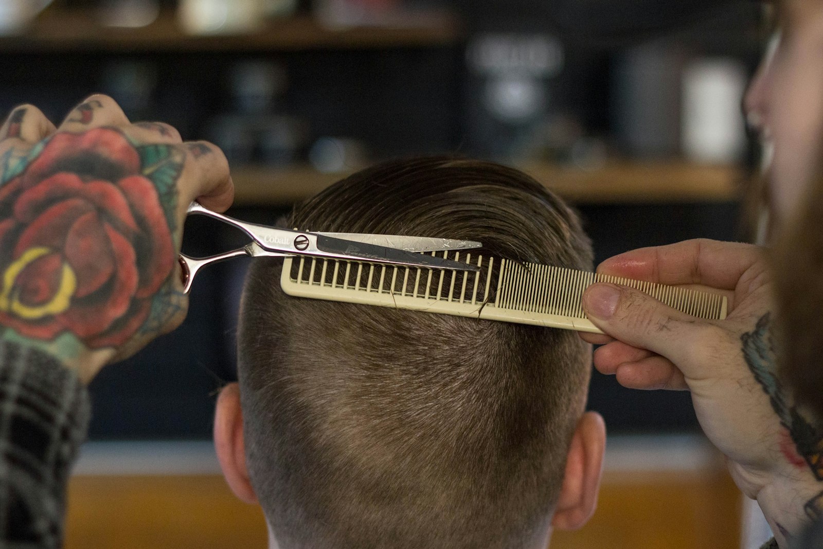 Barber's hands guiding a comb and scissors through a client's hair